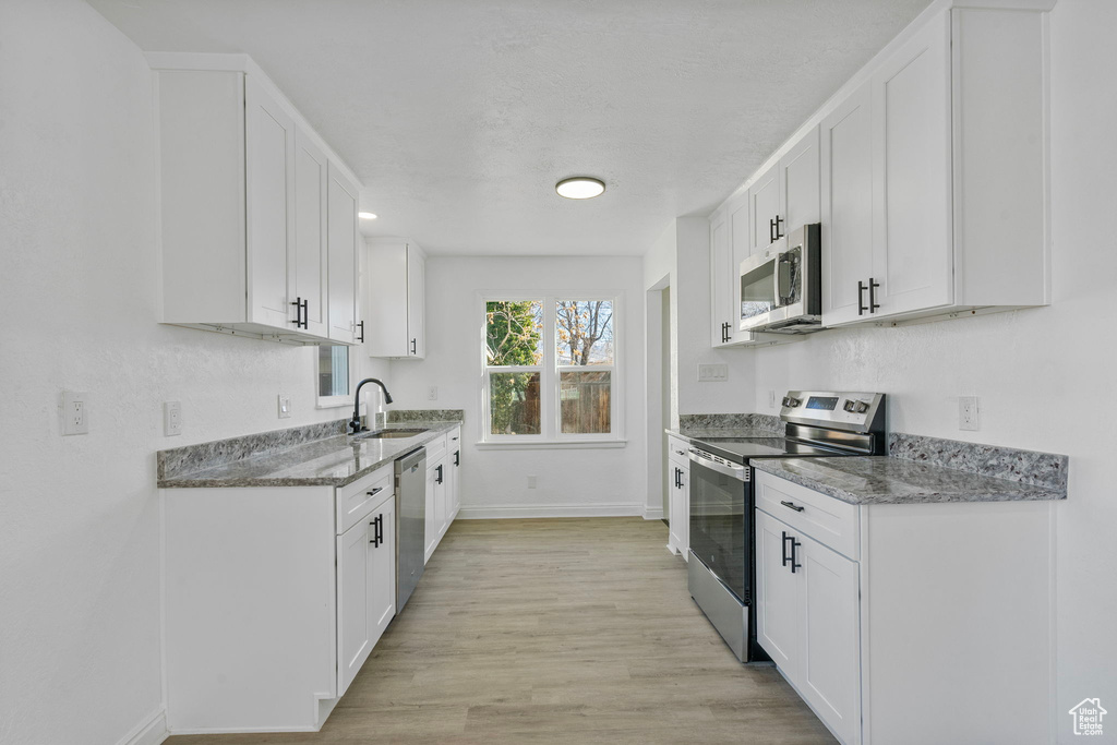 Kitchen featuring sink, light stone counters, light wood-type flooring, appliances with stainless steel finishes, and white cabinets