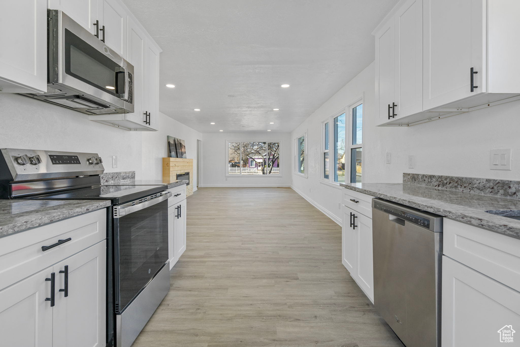 Kitchen featuring light stone counters, light wood-type flooring, white cabinets, and appliances with stainless steel finishes