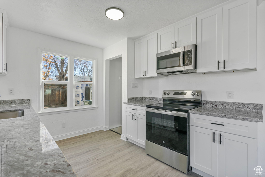 Kitchen featuring white cabinetry, sink, stainless steel appliances, light stone countertops, and light hardwood / wood-style flooring