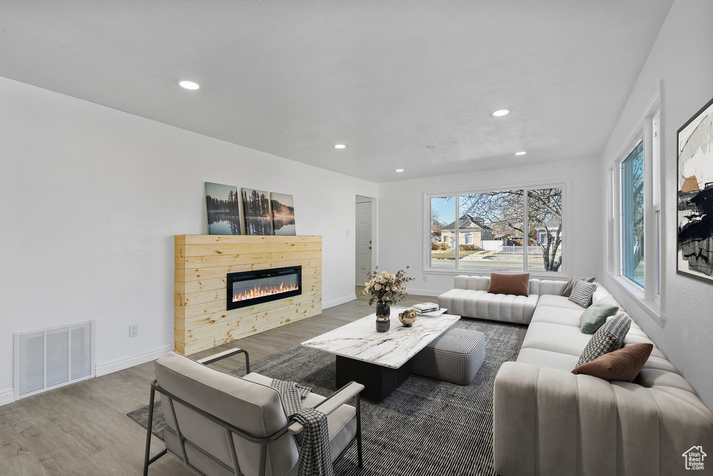 Living room featuring a glass covered fireplace, visible vents, recessed lighting, and wood finished floors