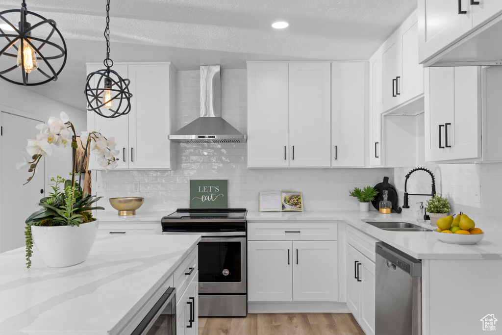 Kitchen featuring sink, appliances with stainless steel finishes, hanging light fixtures, white cabinets, and wall chimney exhaust hood