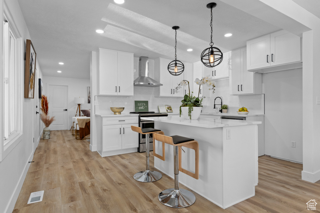 Kitchen with wall chimney range hood, white cabinetry, a kitchen island, decorative backsplash, and stainless steel range with electric cooktop