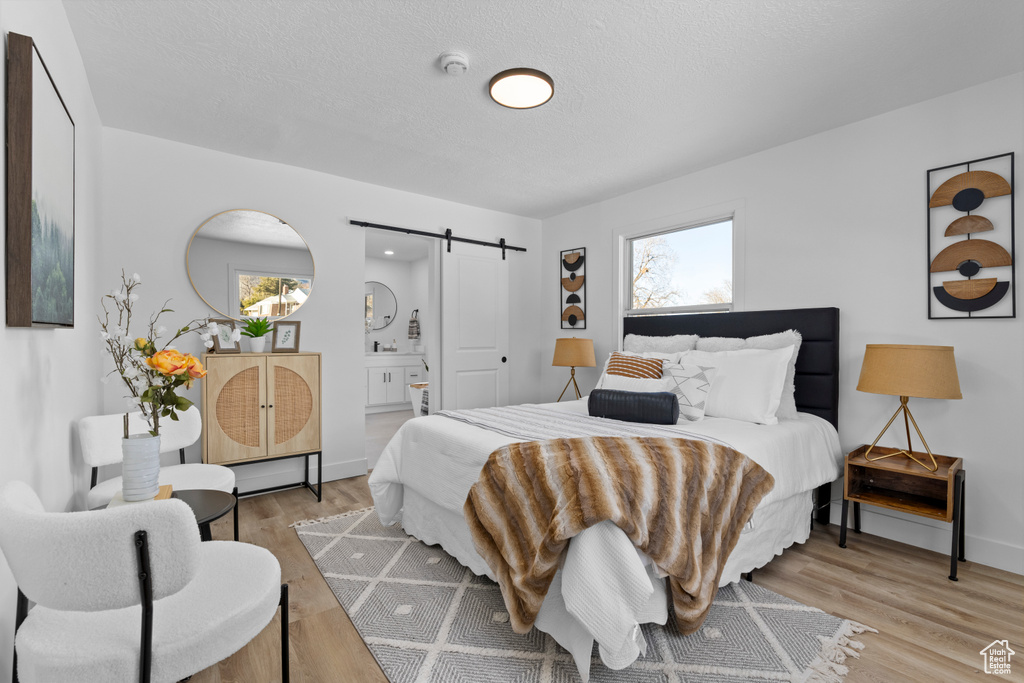 Bedroom with ensuite bathroom, a barn door, light hardwood / wood-style flooring, and a textured ceiling