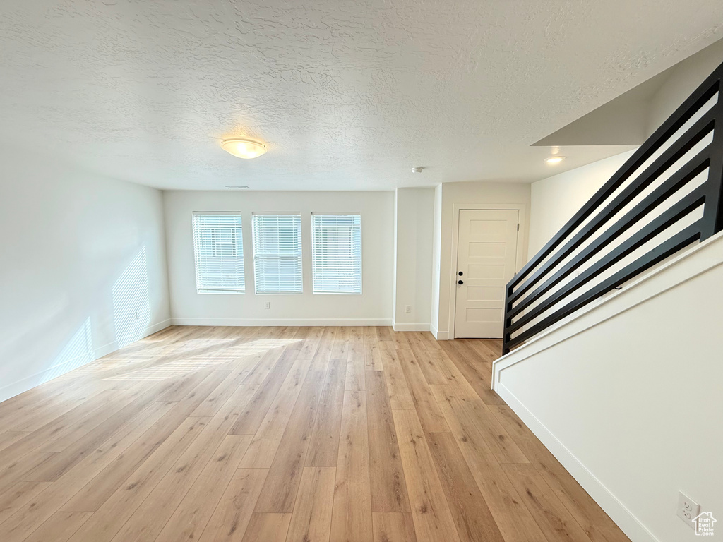 Unfurnished living room featuring baseboards, a textured ceiling, light wood finished floors, and stairs