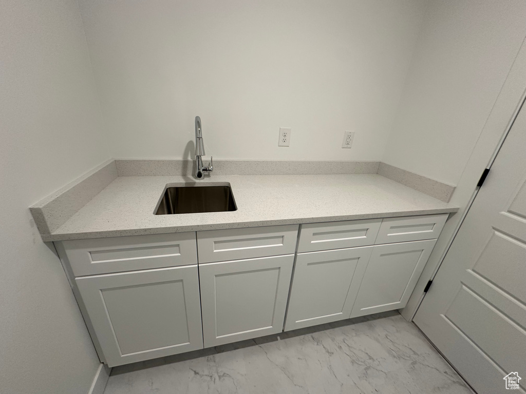 Kitchen featuring light marble finish floors, a sink, and white cabinetry