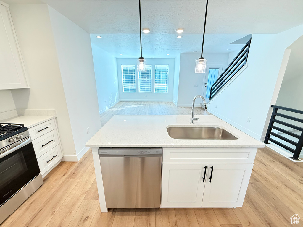 Kitchen with a sink, white cabinets, appliances with stainless steel finishes, light wood-type flooring, and an island with sink