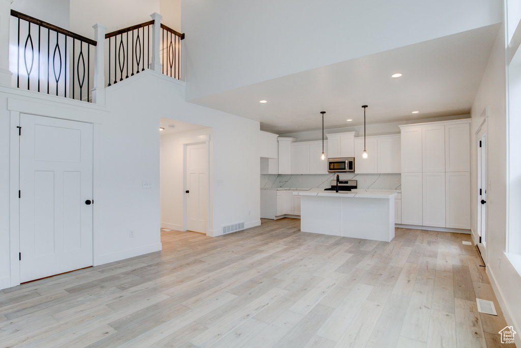 Kitchen with decorative light fixtures, light wood-type flooring, a center island with sink, and white cabinets