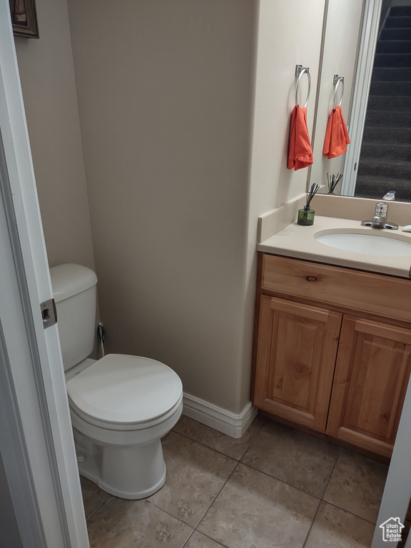 Half bath featuring baseboards, toilet, vanity, and tile patterned flooring