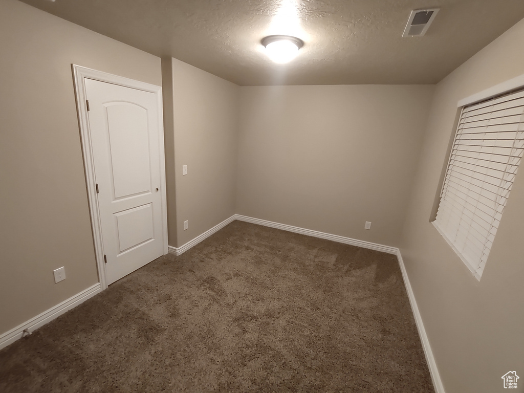 Unfurnished room featuring dark colored carpet, visible vents, baseboards, and a textured ceiling