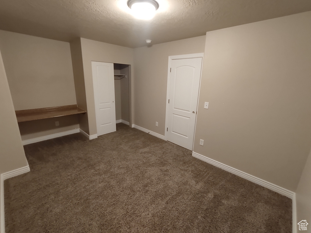 Unfurnished bedroom with a closet, baseboards, a textured ceiling, and dark carpet