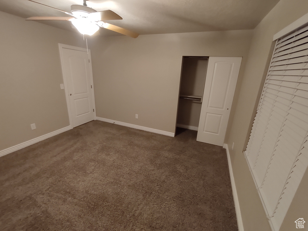 Unfurnished bedroom with a closet, dark carpet, a ceiling fan, and baseboards