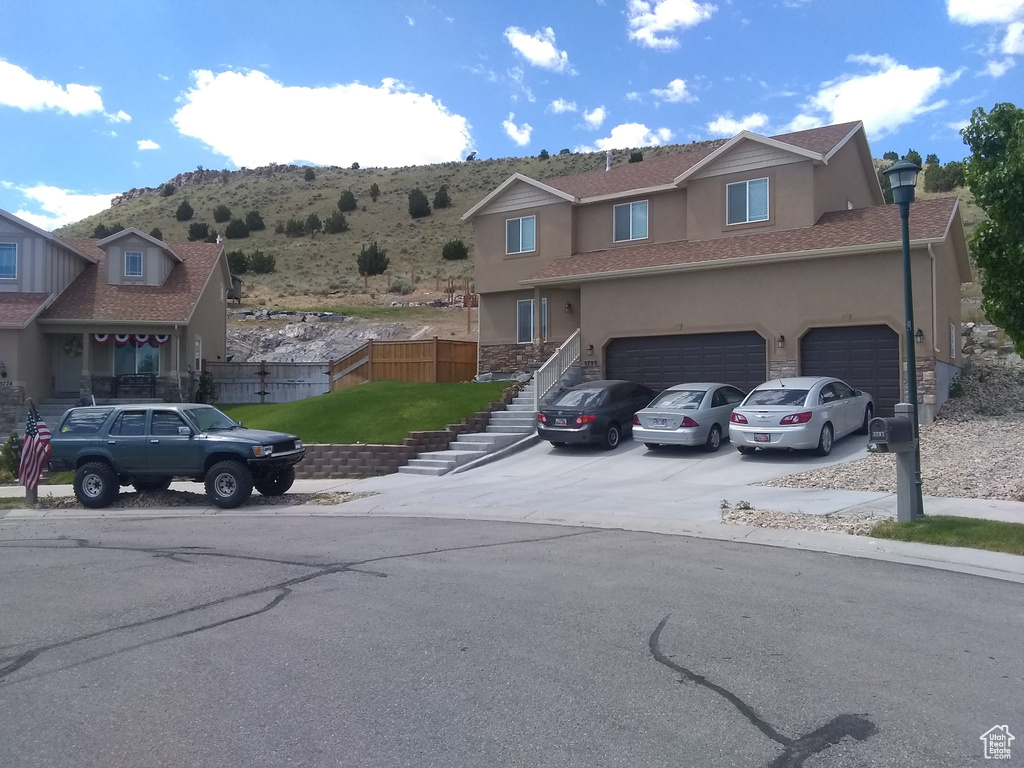 View of front facade featuring stucco siding, driveway, stairs, and fence