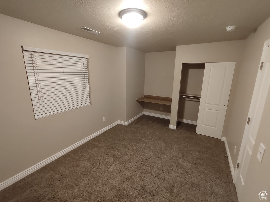 Unfurnished bedroom with baseboards, visible vents, a closet, a textured ceiling, and dark carpet