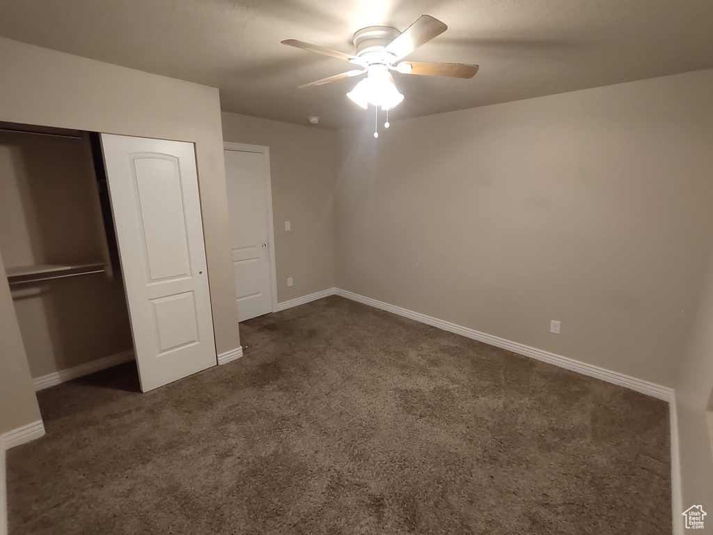 Unfurnished bedroom featuring a closet, ceiling fan, baseboards, and dark colored carpet