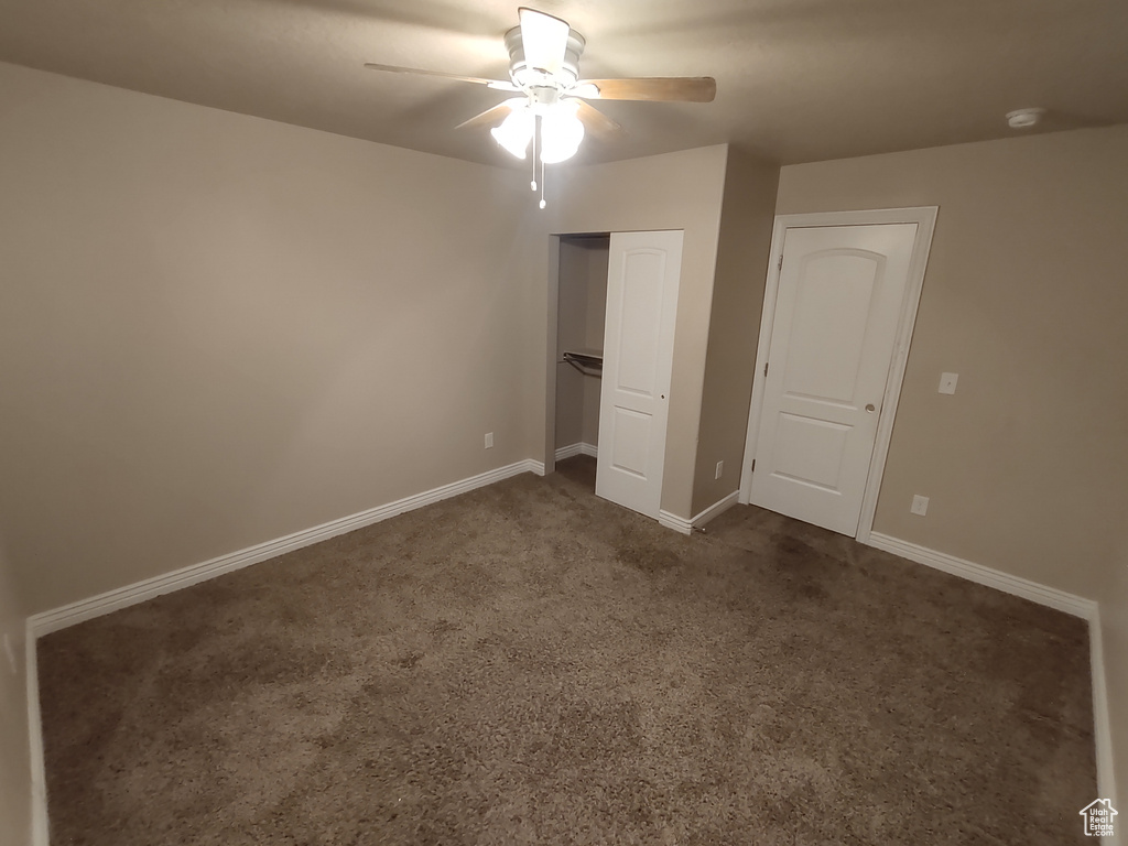 Unfurnished bedroom featuring dark colored carpet, a closet, baseboards, and a ceiling fan