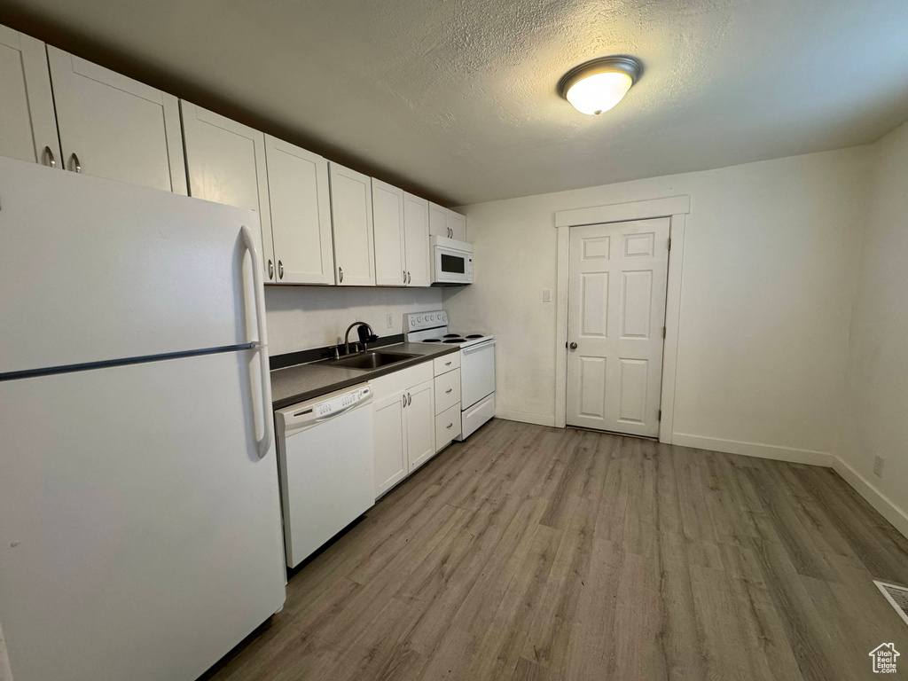 Kitchen with white cabinetry, sink, white appliances, and light hardwood / wood-style flooring