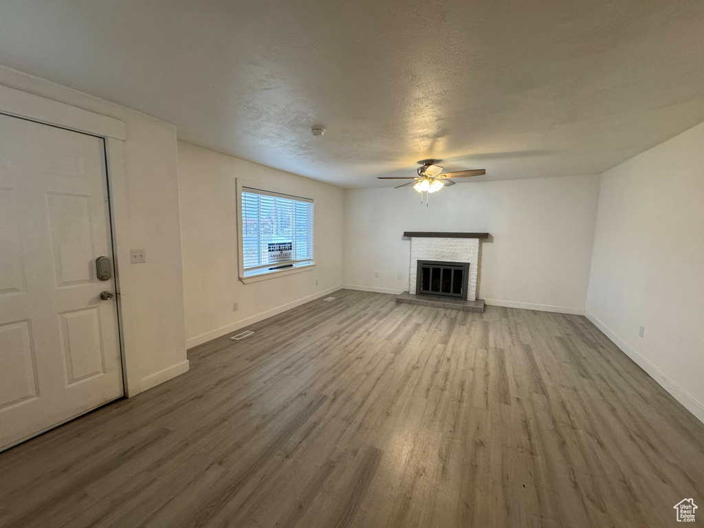 Unfurnished living room with ceiling fan, hardwood / wood-style flooring, a fireplace, and a textured ceiling