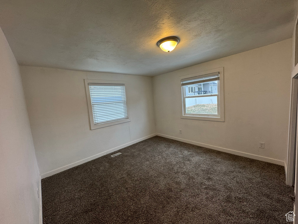 Empty room featuring dark colored carpet and a textured ceiling
