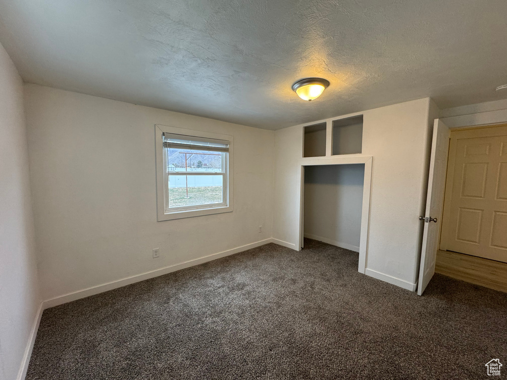 Unfurnished bedroom featuring a closet, a textured ceiling, and dark colored carpet