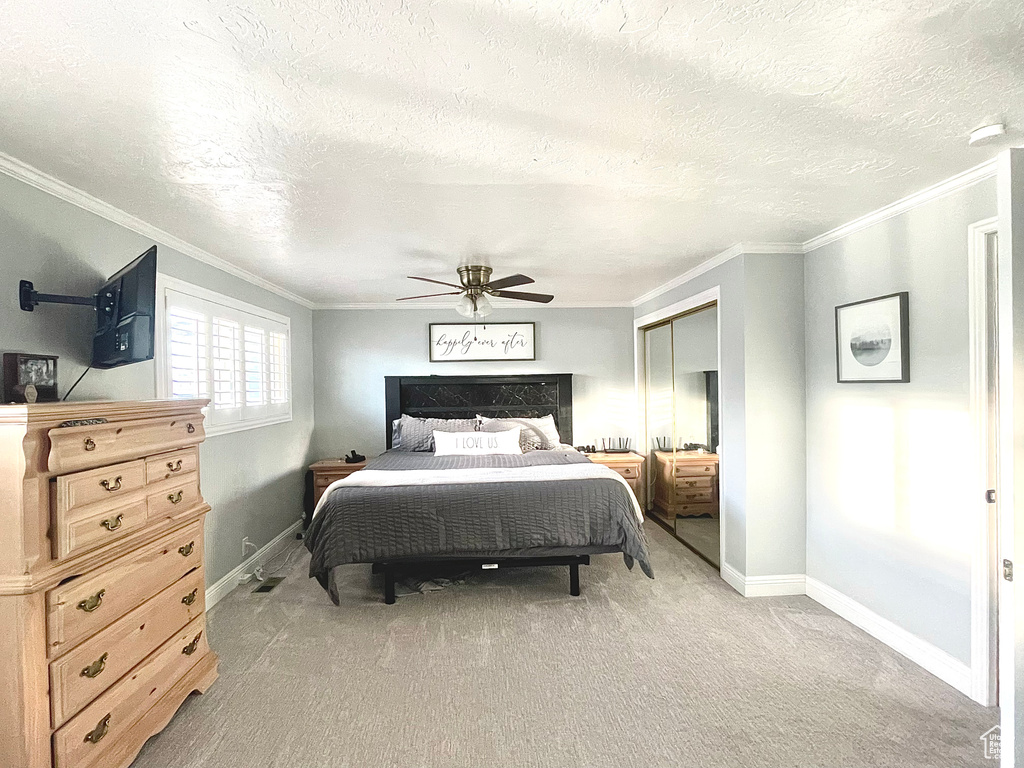 Bedroom with ceiling fan, ornamental molding, a textured ceiling, light carpet, and a closet