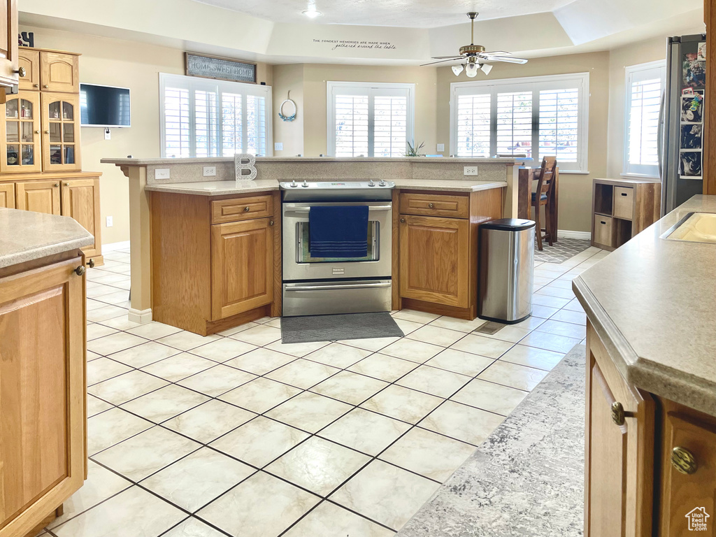 Kitchen featuring appliances with stainless steel finishes, a raised ceiling, a kitchen island with sink, and light tile patterned floors