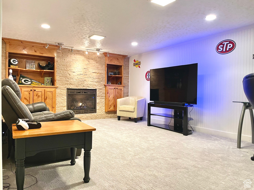 Carpeted living room featuring a stone fireplace, a textured ceiling, and built in shelves