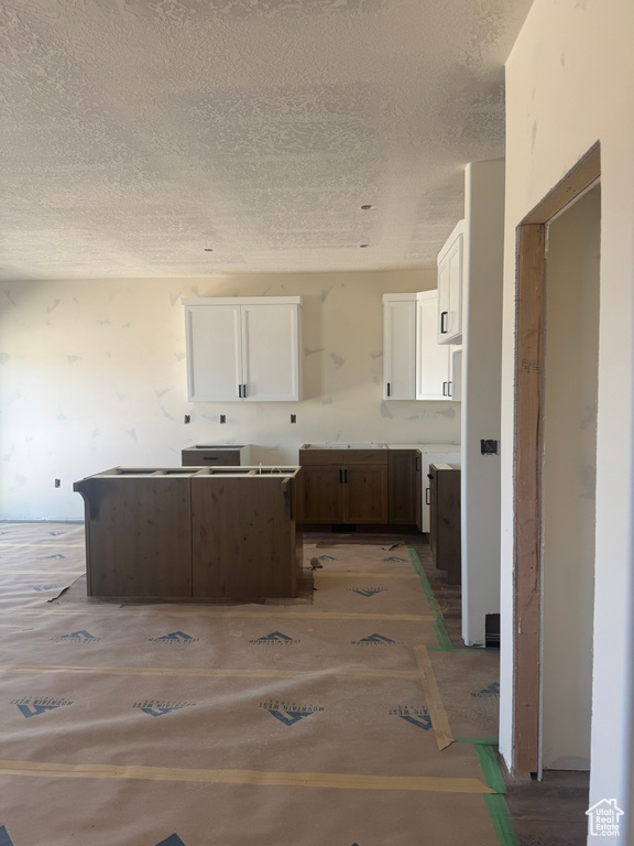 Kitchen with a sink, a kitchen island, a textured ceiling, and white cabinetry