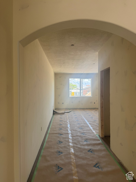Hallway featuring arched walkways and a textured ceiling