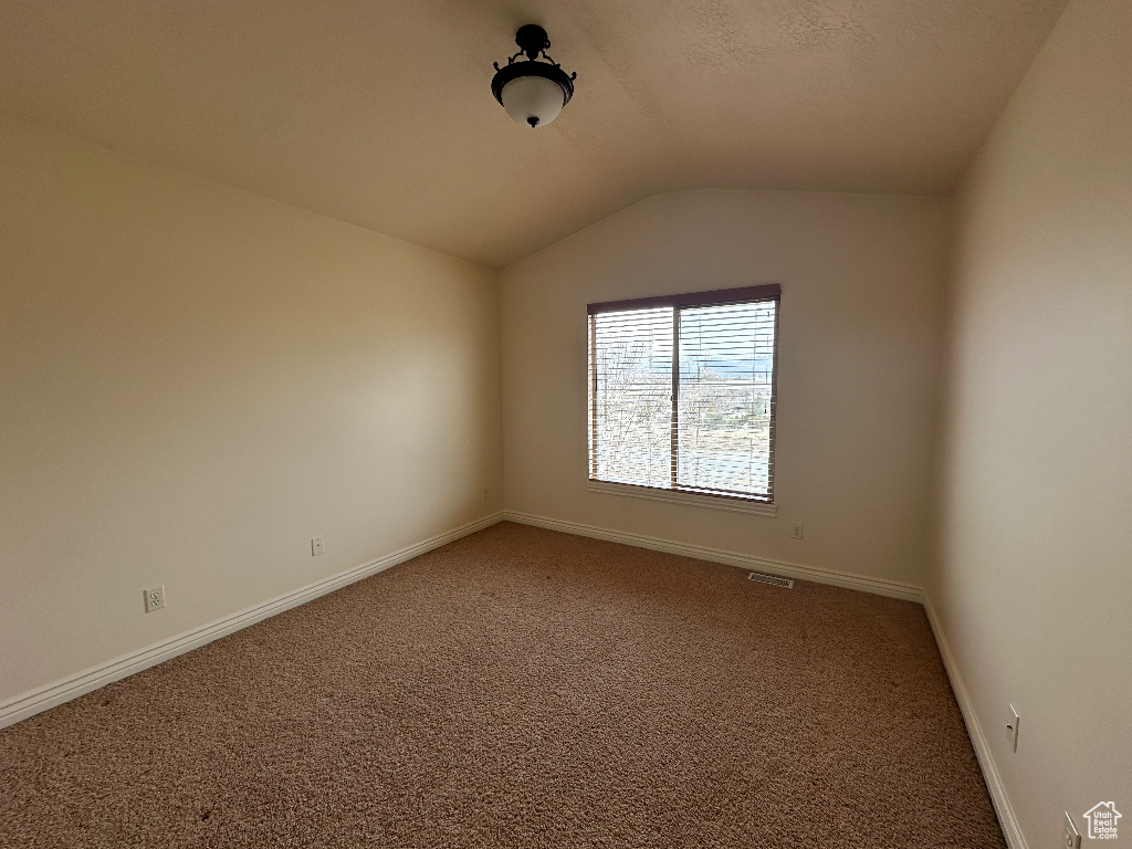 Empty room featuring lofted ceiling and carpet flooring