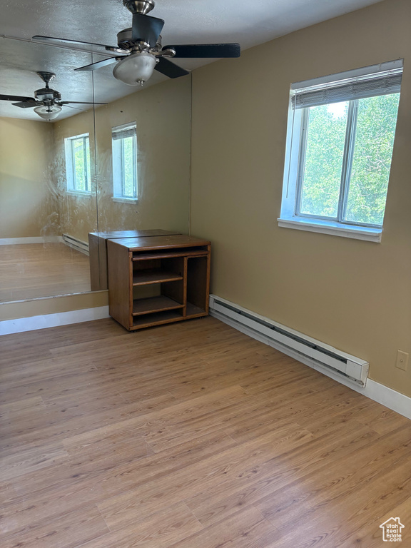 Unfurnished room featuring a baseboard heating unit, a ceiling fan, baseboards, and wood finished floors