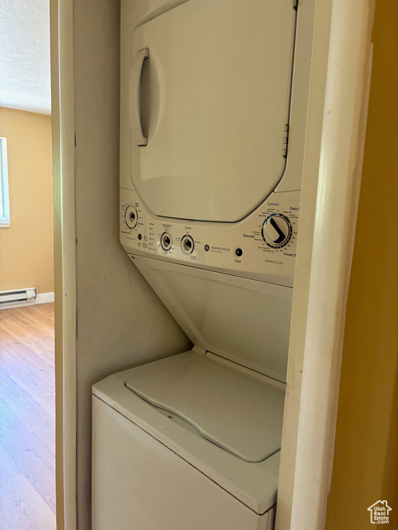 Laundry area with stacked washer / drying machine, wood finished floors, and a baseboard radiator