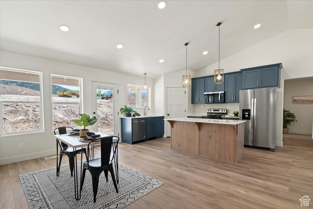 Kitchen featuring lofted ceiling, stainless steel appliances, light countertops, a center island, and blue cabinetry