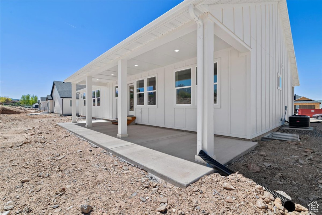 Rear view of house with central AC, board and batten siding, and a patio