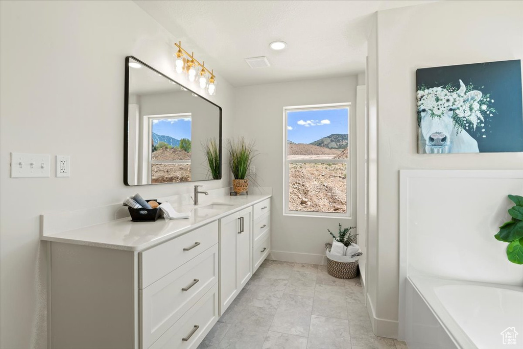 Bathroom featuring plenty of natural light, visible vents, vanity, and a tub to relax in