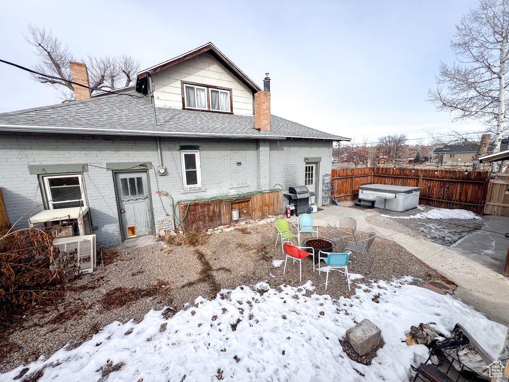 Snow covered back of property featuring a hot tub