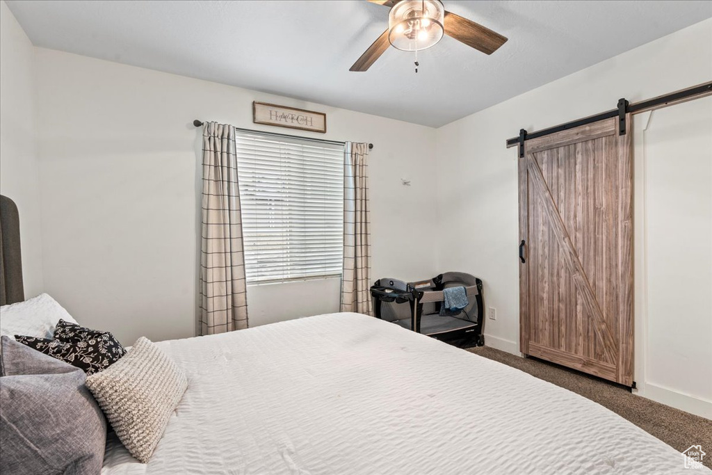 Bedroom featuring ceiling fan, a barn door, and dark colored carpet