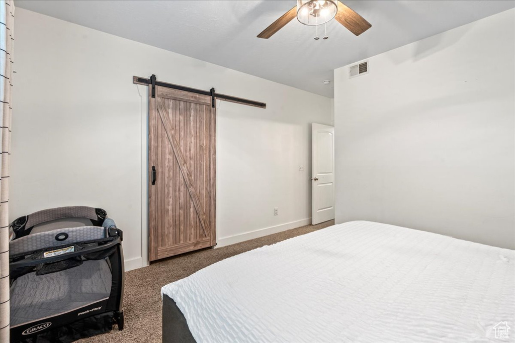 Bedroom featuring ceiling fan, a barn door, and dark colored carpet