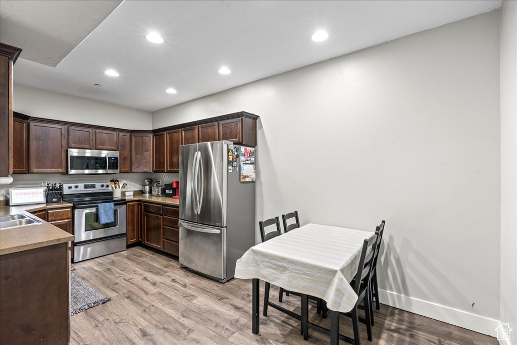 Kitchen with appliances with stainless steel finishes, sink, light hardwood / wood-style floors, and dark brown cabinets