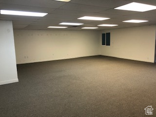 Empty room with a drop ceiling and dark colored carpet