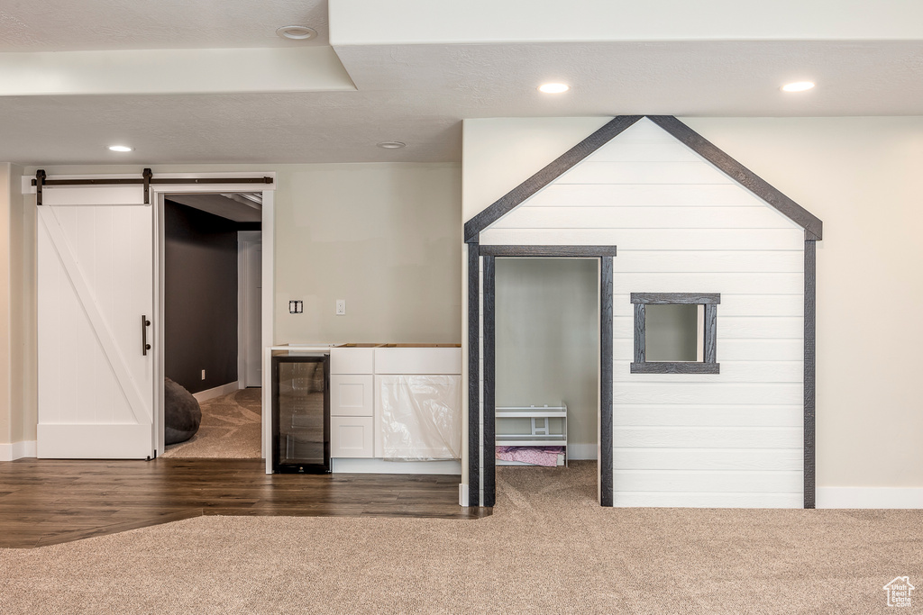 Interior space with wine cooler, a barn door, and dark colored carpet