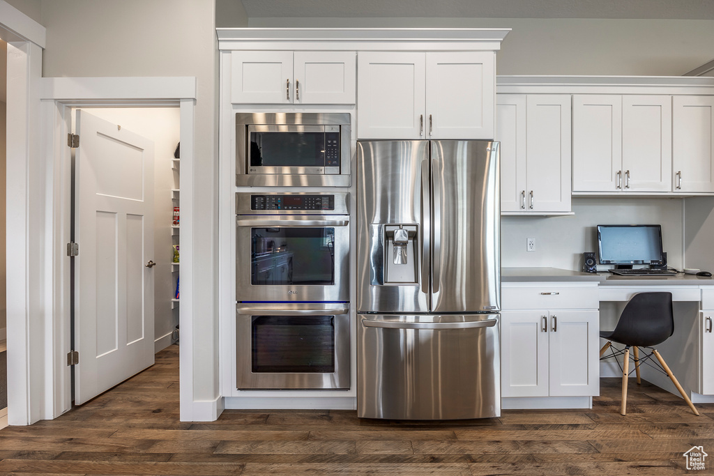 Kitchen with white cabinetry, stainless steel appliances, dark hardwood / wood-style floors, and built in desk