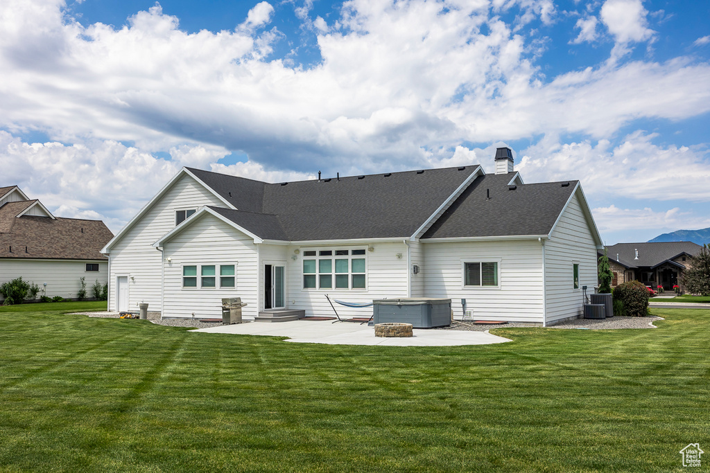 Back of property with a lawn, a hot tub, a patio, and central air condition unit