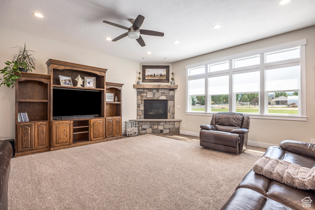 Carpeted living room featuring ceiling fan, a stone fireplace, and a textured ceiling