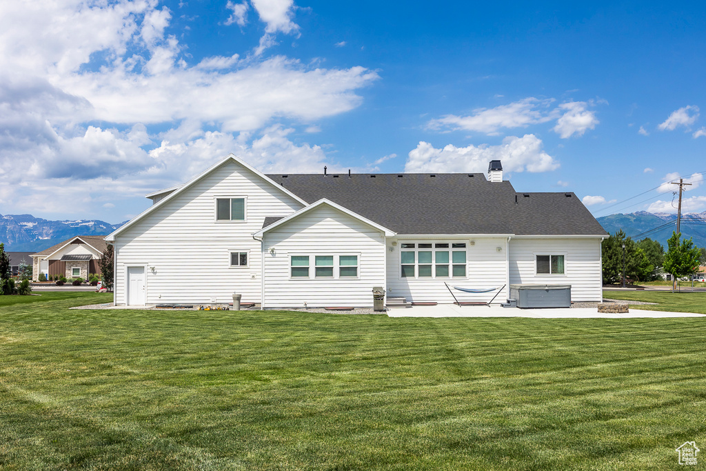 Rear view of property featuring a hot tub, a mountain view, a yard, and a patio area