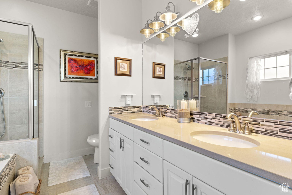 Bathroom with a shower with shower door, backsplash, vanity, toilet, and tile patterned floors