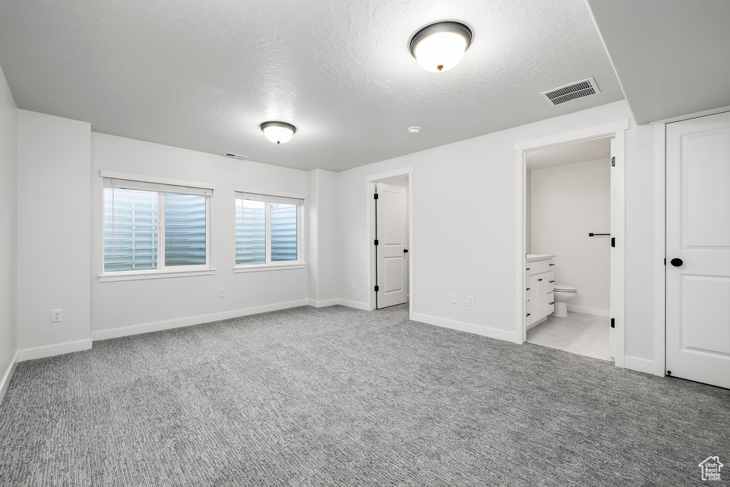 Unfurnished bedroom with ensuite bath, light colored carpet, and a textured ceiling