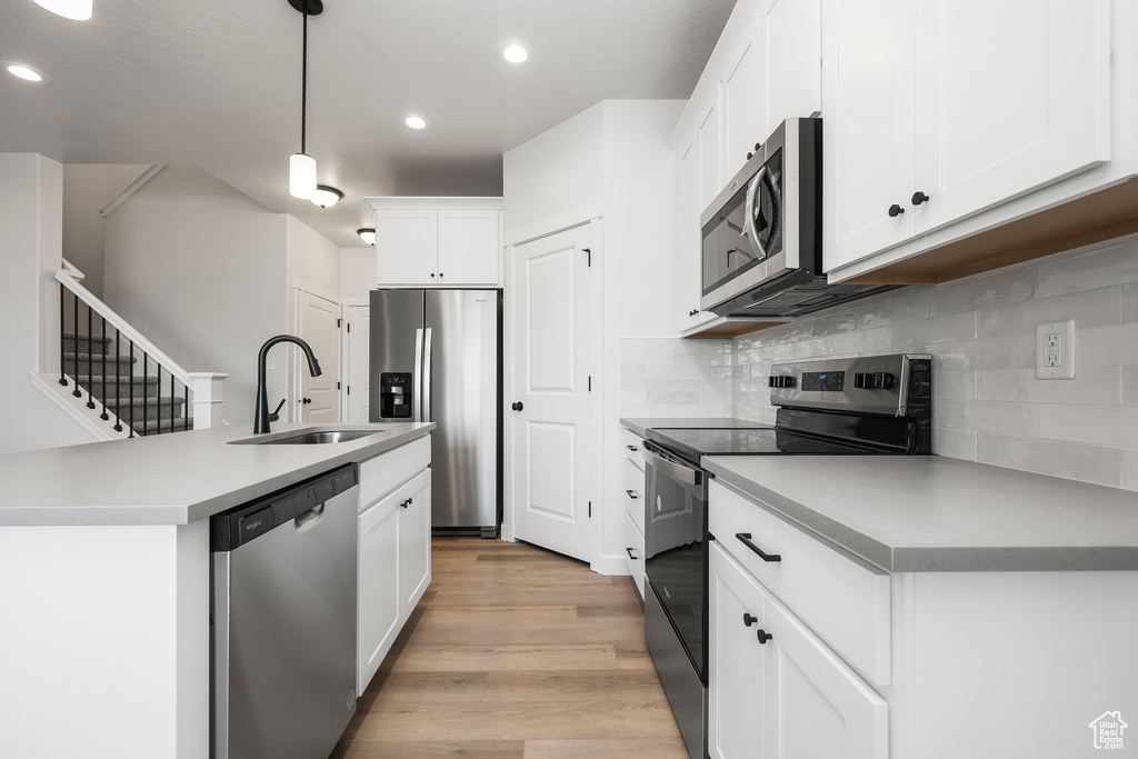 Kitchen with tasteful backsplash, white cabinetry, sink, hanging light fixtures, and stainless steel appliances