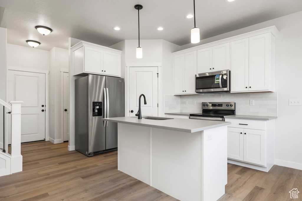 Kitchen with white cabinetry, stainless steel appliances, sink, and hanging light fixtures