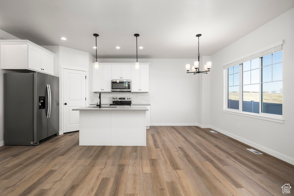 Kitchen with white cabinetry, wood-type flooring, an island with sink, hanging light fixtures, and stainless steel appliances