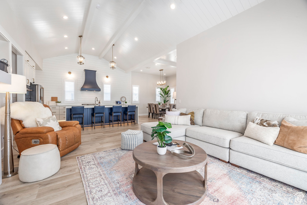 Living room with vaulted ceiling with beams, a notable chandelier, light hardwood / wood-style flooring, and sink